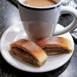 two slices of nut roll and a cup of coffee on white dessert plate