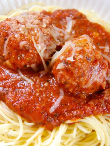 spaghetti with red sauce and two meatballs on white plate