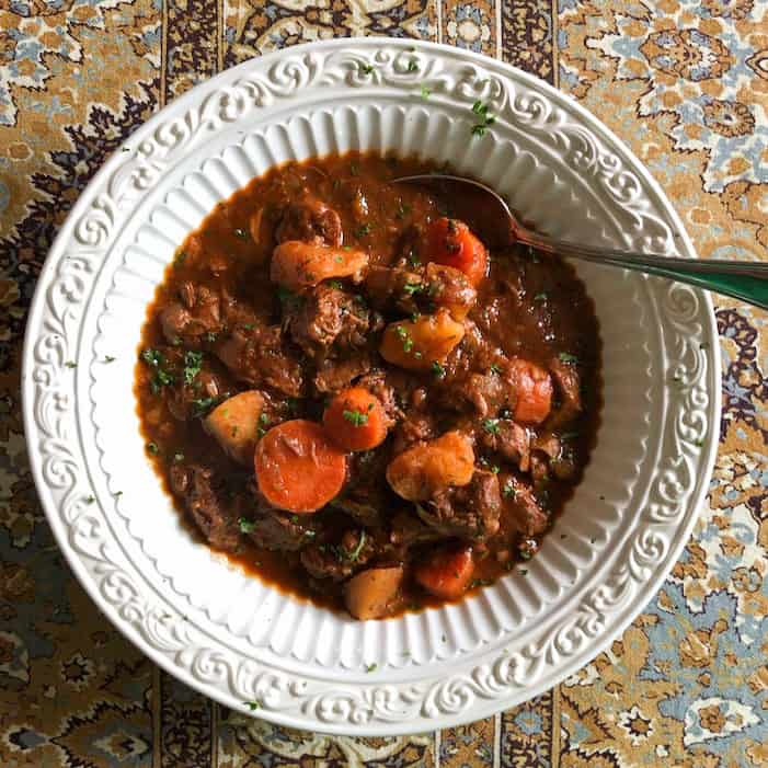 dark brown guinness beef stew with carrots and potatoes in white bowl with spoon