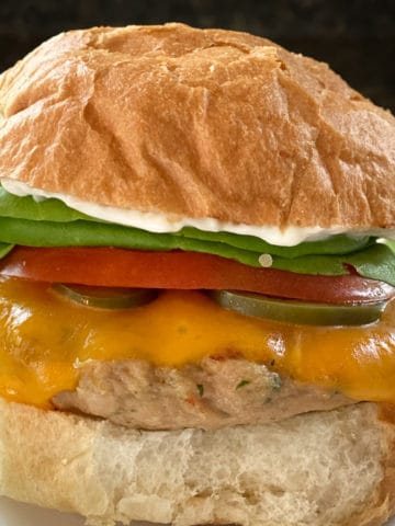 grilled turkey burger on bun with melted cheddar cheese, lettuce, tomato, pickle, and mayo