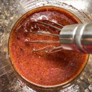 overhead view of kalamata vinaigrette in measuring cup with whisk