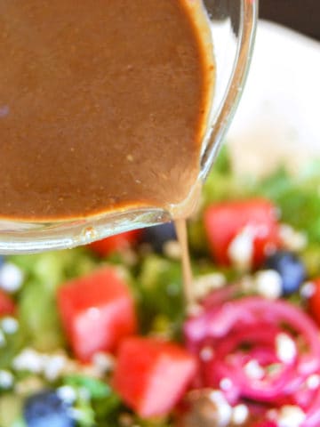 balsamic vinaigrette drizzled out of glass measuring up onto watermelon and blueberry salad