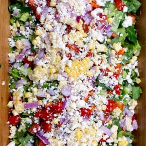 summer salad of chopped romaine, red peppers, purple onion, fresh corn, and cotilla cheese in wooden bowl