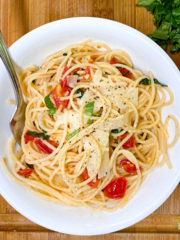 white bowl of spaghetti with fresh chopped tomatoes and basil, topped with shaved parmesan