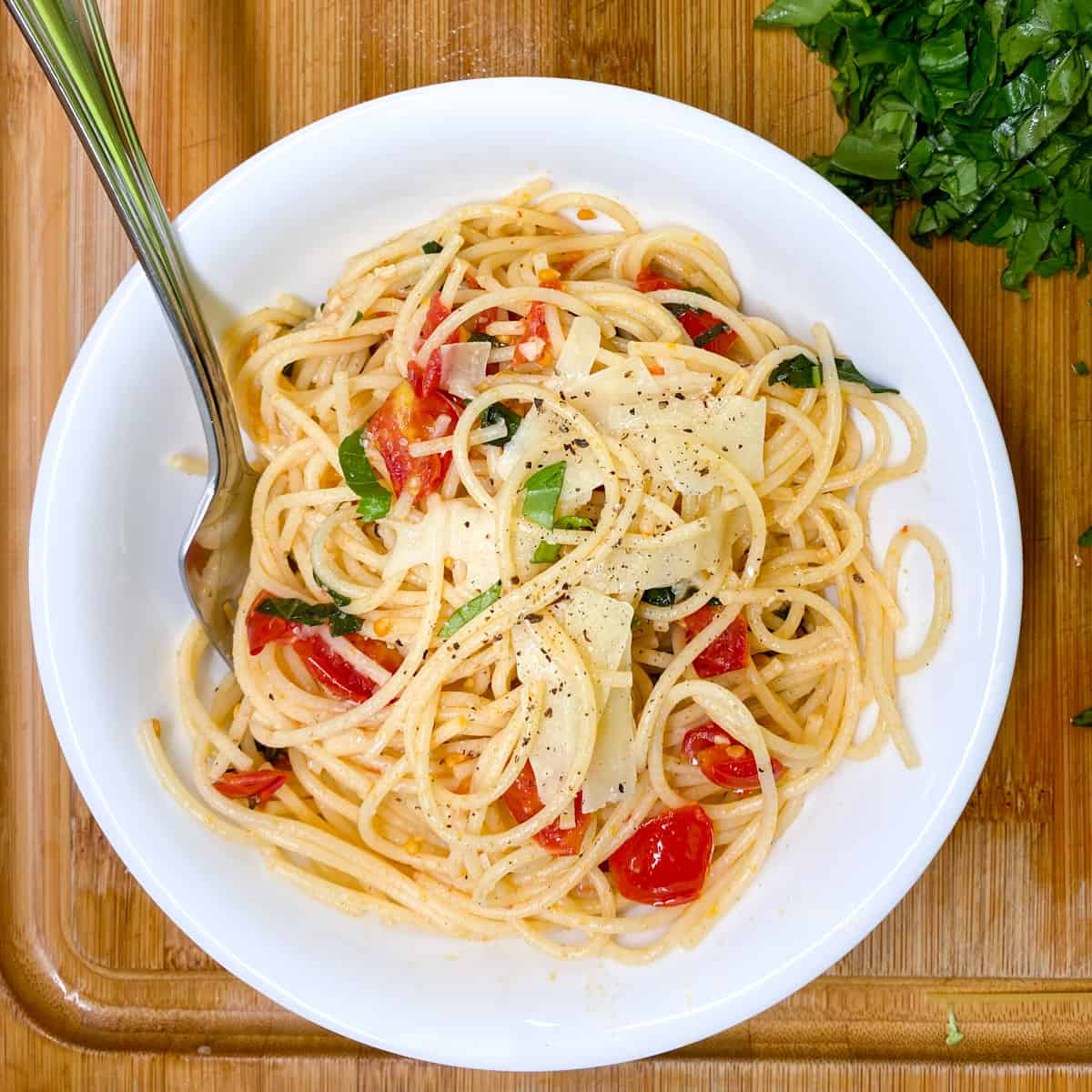 white bowl of spaghetti with fresh chopped tomatoes and basil, topped with shaved parmesan