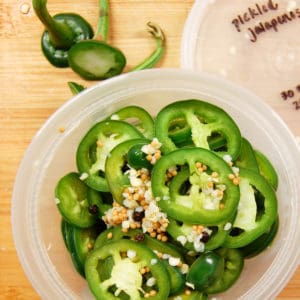 fresh sliced jalapeño peppers and pickling spices in plastic container