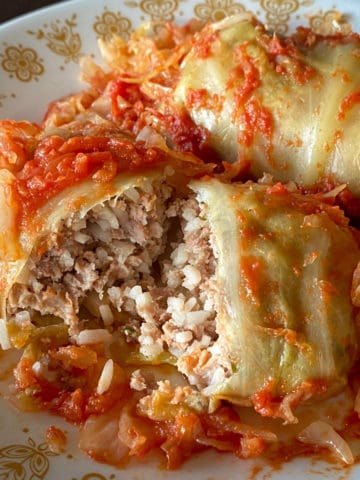 two cabbage rolls on plate with one cut open to see ground meat and rice filling