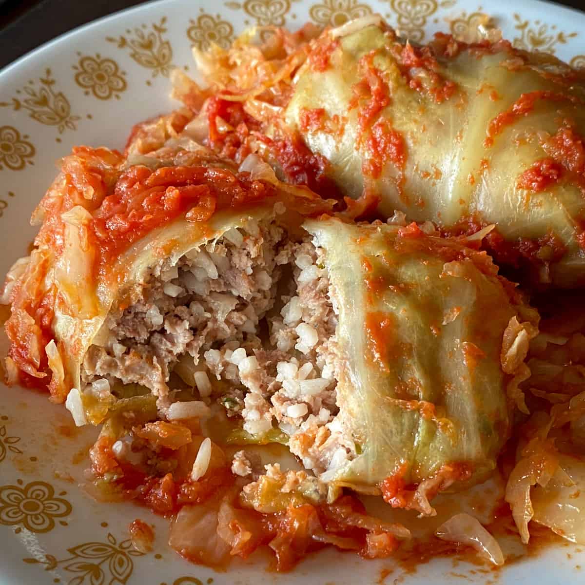 two cabbage rolls on plate with one cut open to see ground meat and rice filling