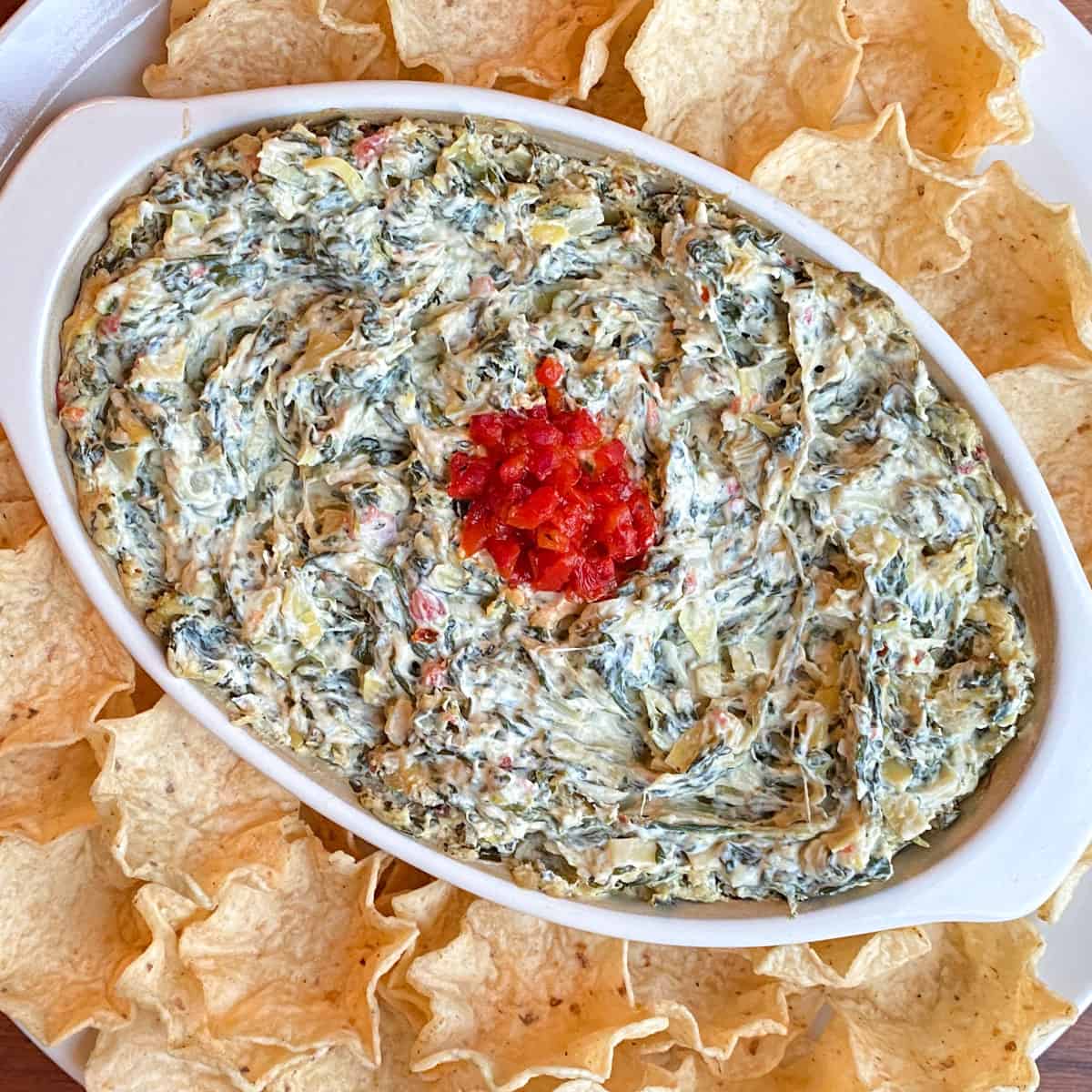 spinach artichoke dip in oval baker surrounded by tortilla chips