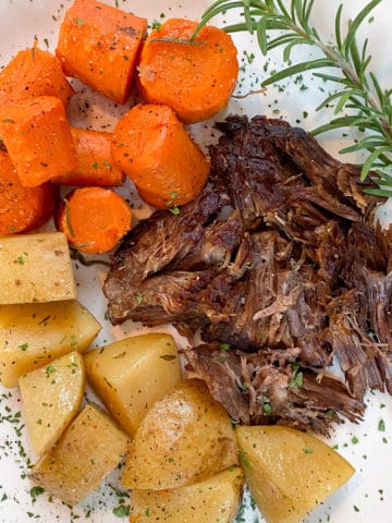 roasted potatoes, carrots, and pot roast on white plate