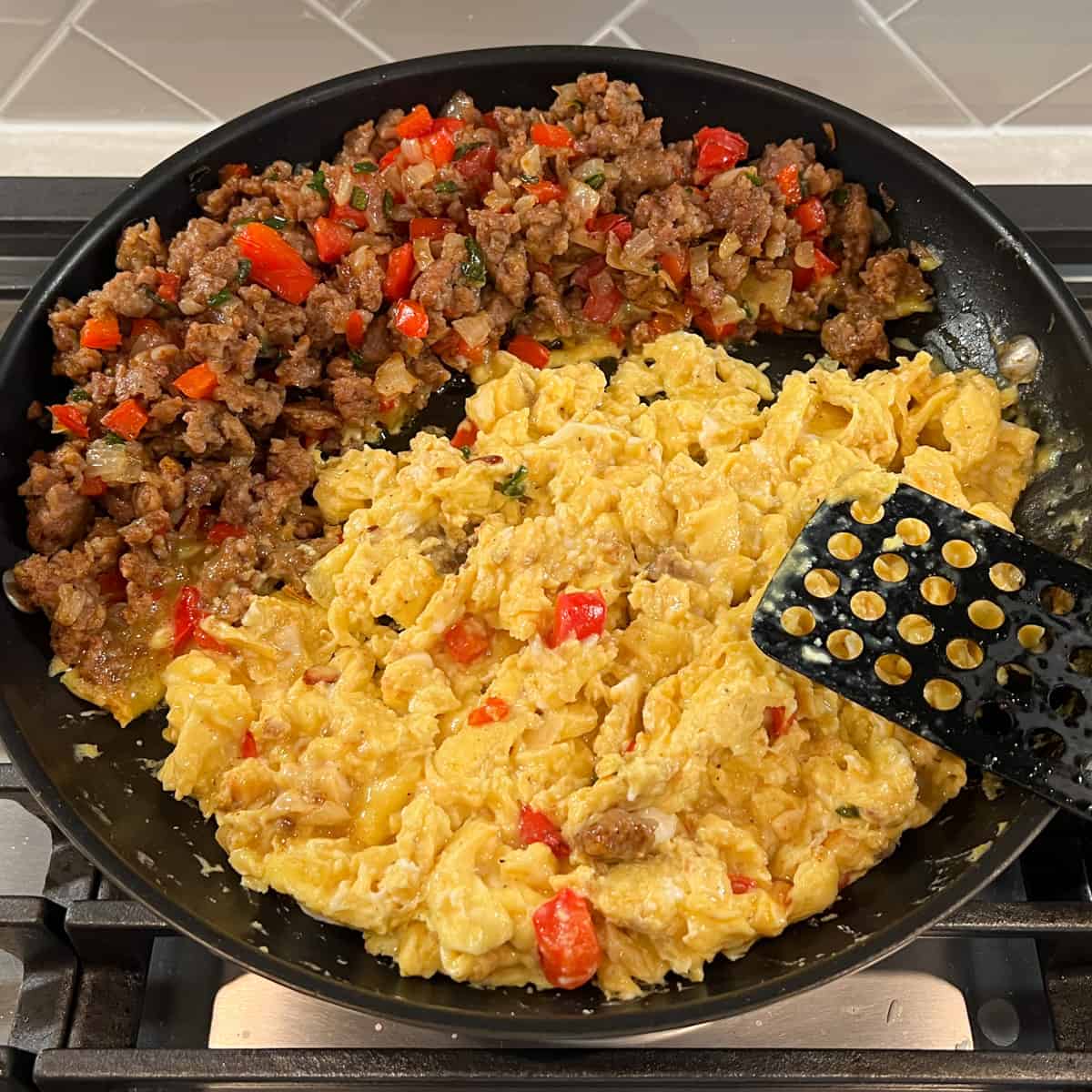 southwest breakfast skillet with browned sausage and chopped peppers and onions pushed to one side while eggs scramble in other side