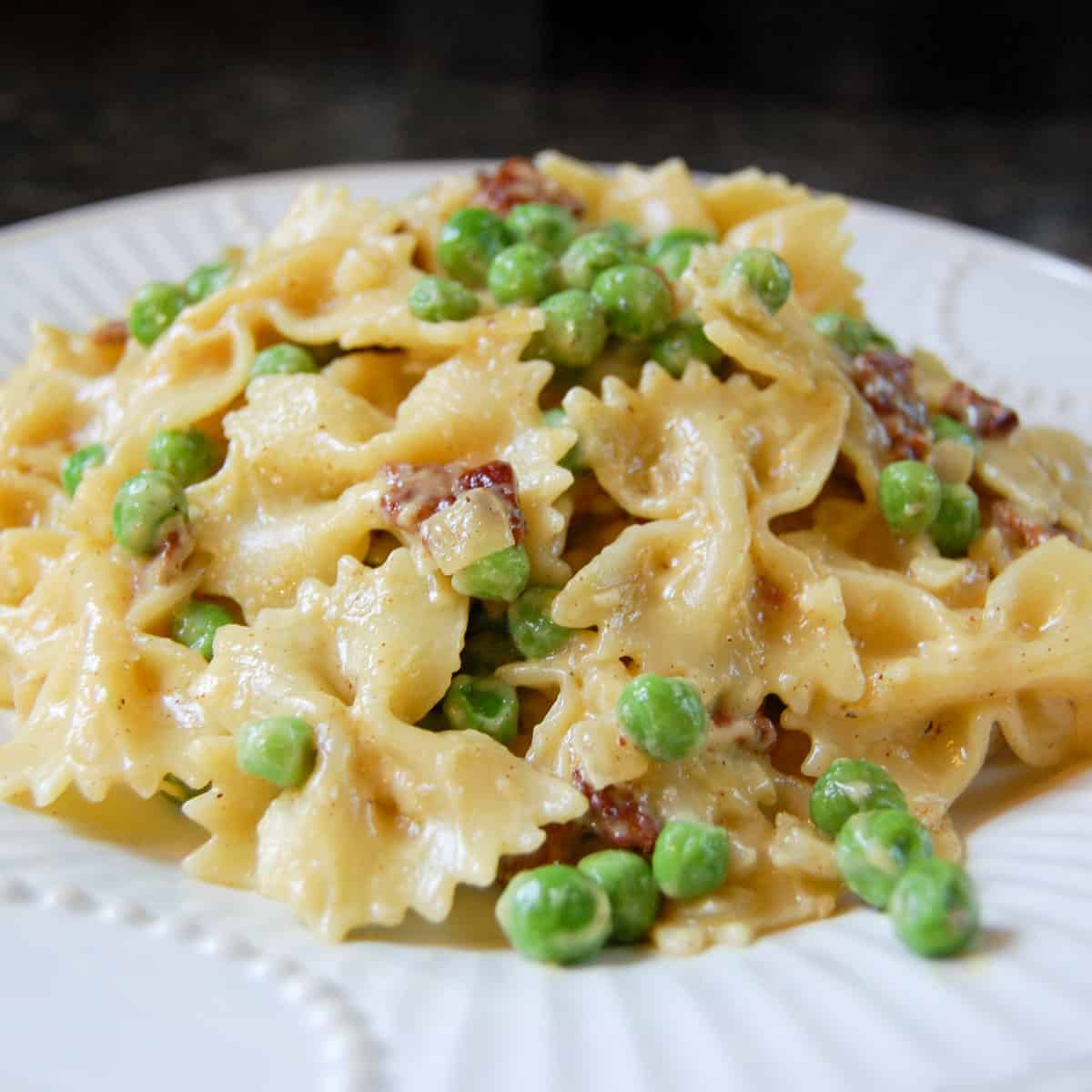 pasta carbonara with bowtie pasta, peas, and chopped bacon on white plate