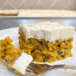 piece of pumpkin cake with creamy white icing on plate with fork