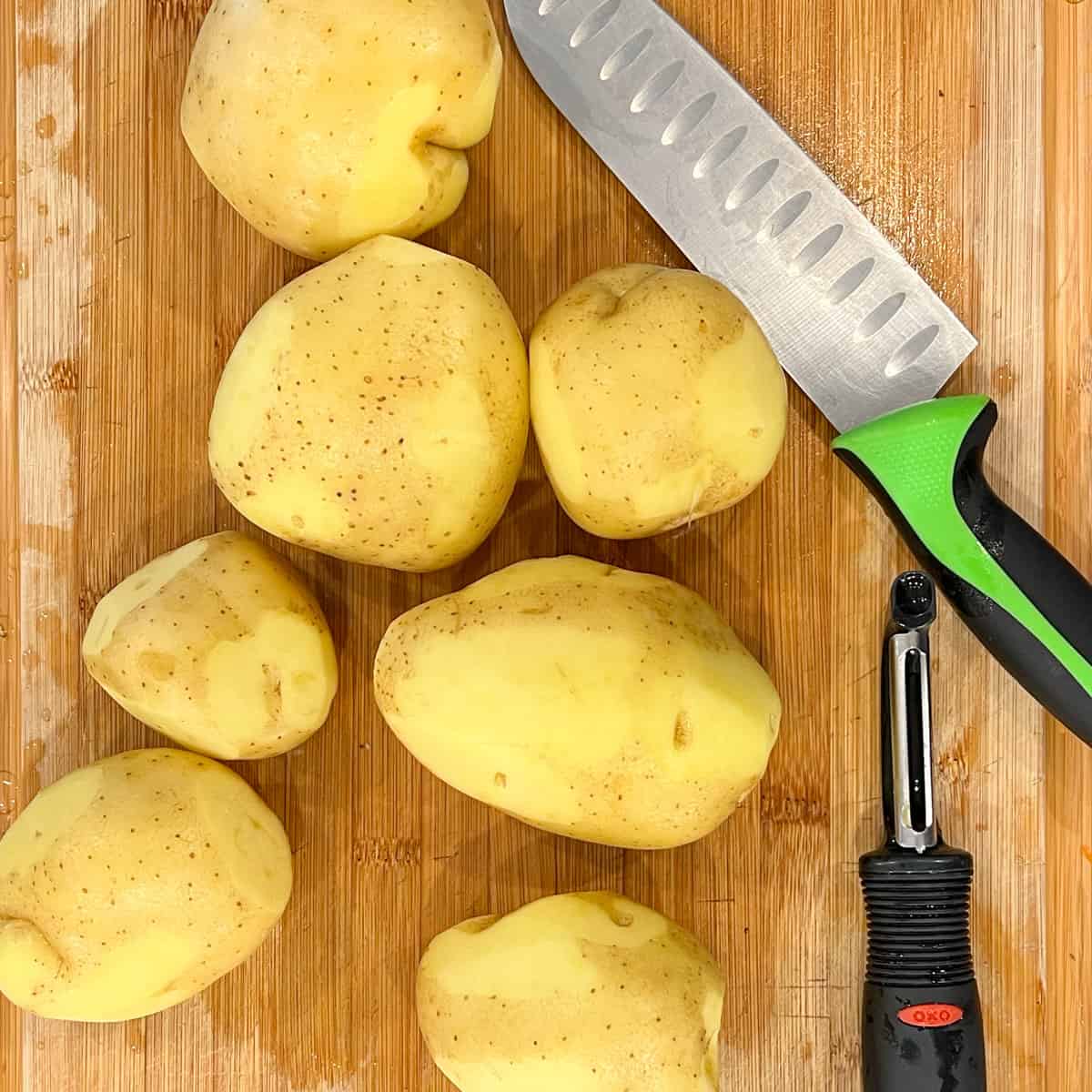 whole yukon gold potatoes on cutting board with peeler and chef's knife
