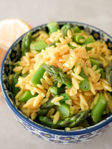 yellow orzo pasta and bright green asparagus pieces in blue flowered bowl