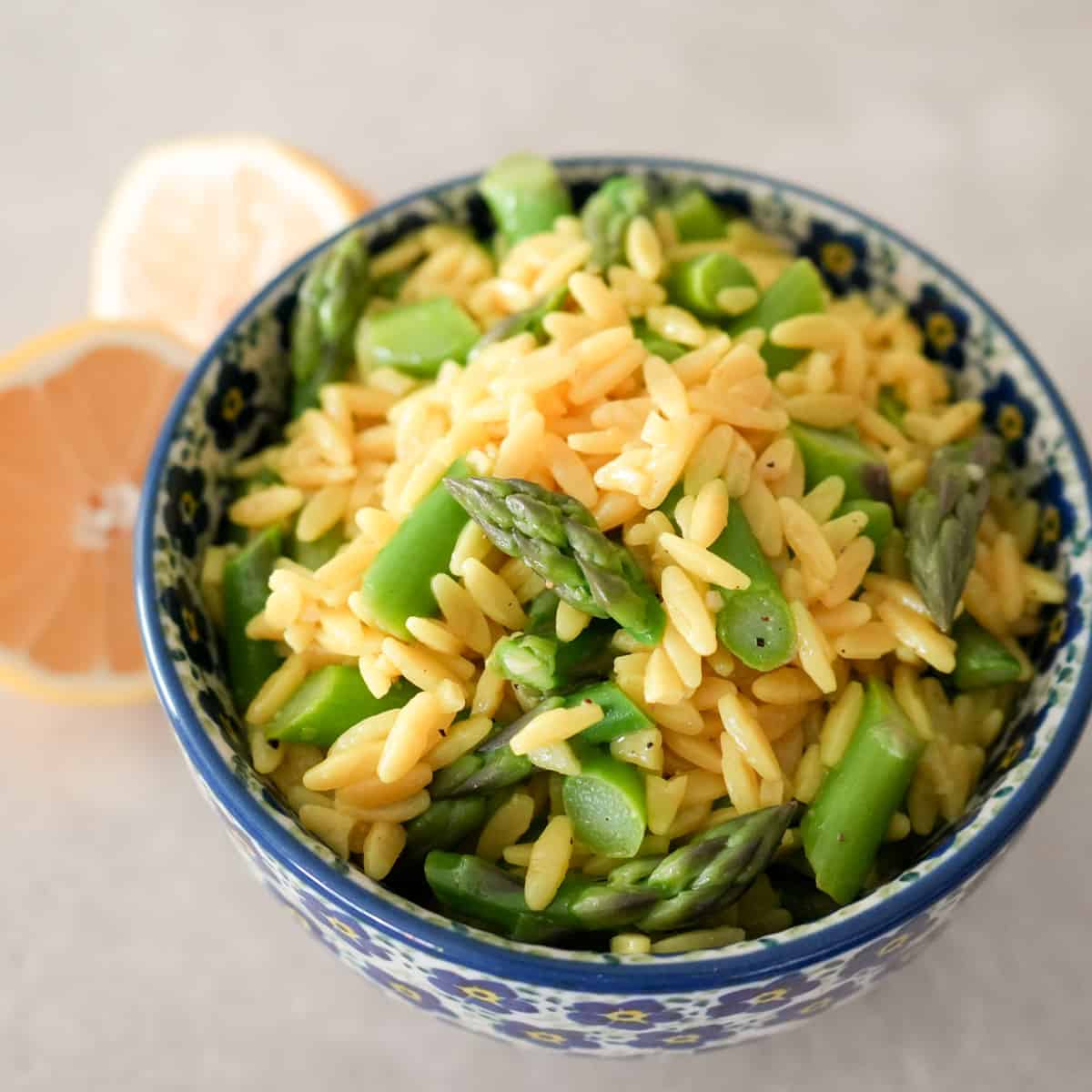 yellow orzo pasta and bright green asparagus pieces in blue flowered bowl