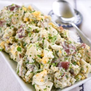 red-skinned potato salad with hard boiled eggs sprinkled with chopped parsley on a rectangular platter